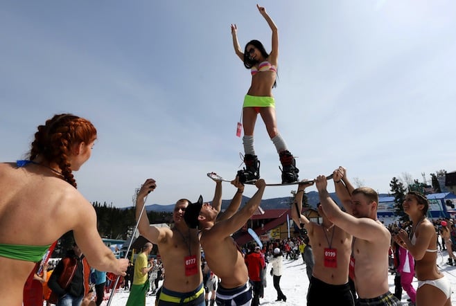 Men hold a woman on a snowboard as they pose for a picture after finishing a "downhill ski and snowboard descent in swimwear" event on Mount Zelyonaya, at a ski resort near the town of Sheregesh