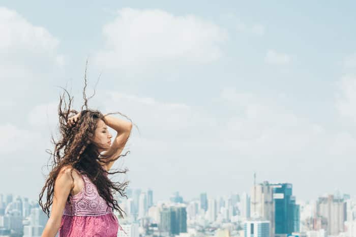 Beautiful woman enjoys the wind on the roof of a tall building with the cityscape in the background.
