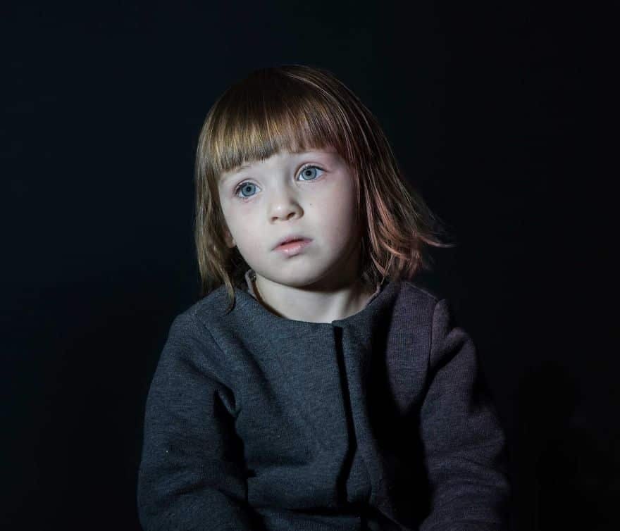 Portrait of girl in grey jacket vacantly staring. She is engrossed in TV.