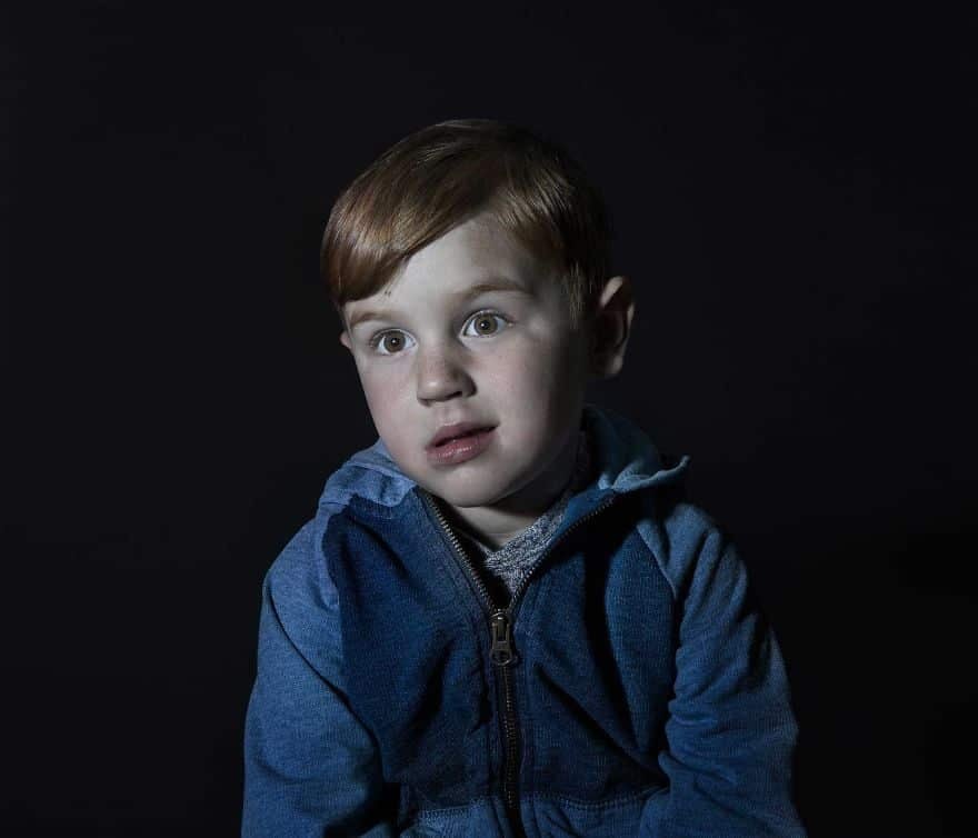 Portrait of a red head boy in blue sweater vacantly staring. He is engrossed in TV.