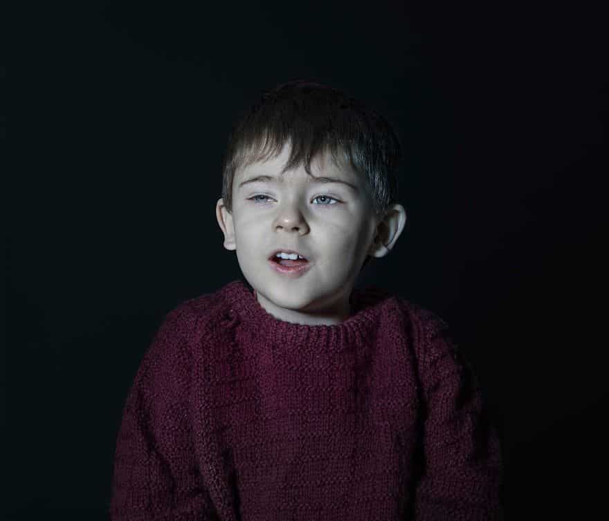 Portrait of a boy in red sweater vacantly staring. He is engrossed in TV.
