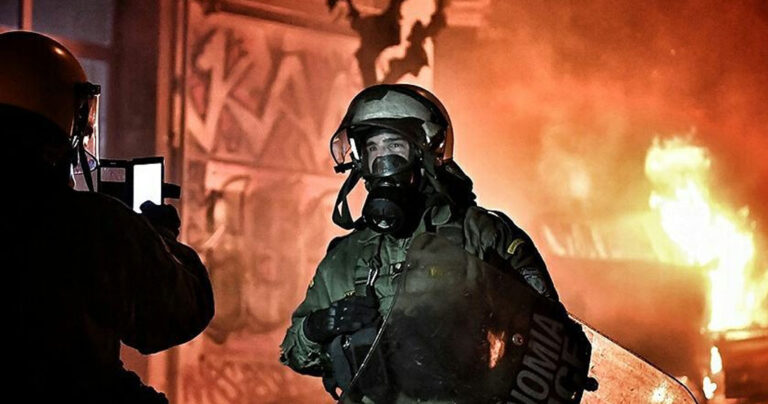 Aνδρας των ΜΑΤ πόζαρε μπροστά σε φλεγόμενους κάδους