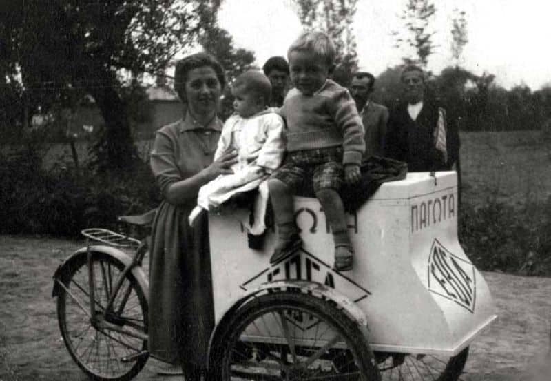 Απεικονίζεται μια γυναίκα με τα δυο παιδιά της να κάθονται πάνω στο καροτσάκι του παγωτού και από πίσω φαίνονται 3 άνδρες