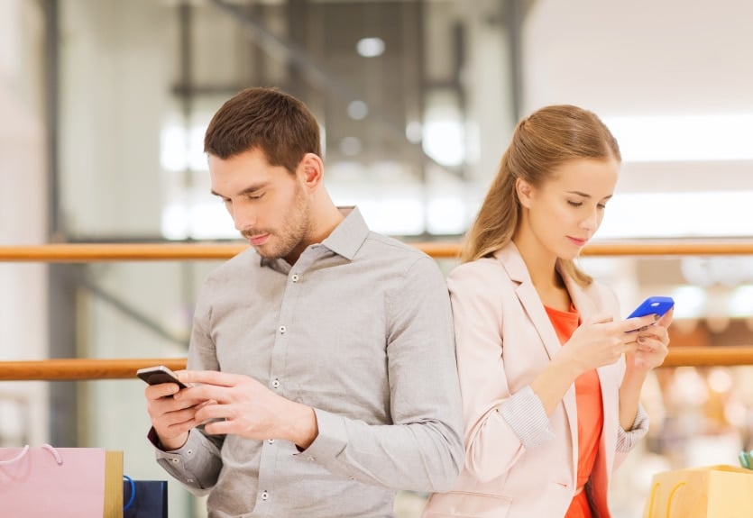 couple with smartphones and shopping bags in mall