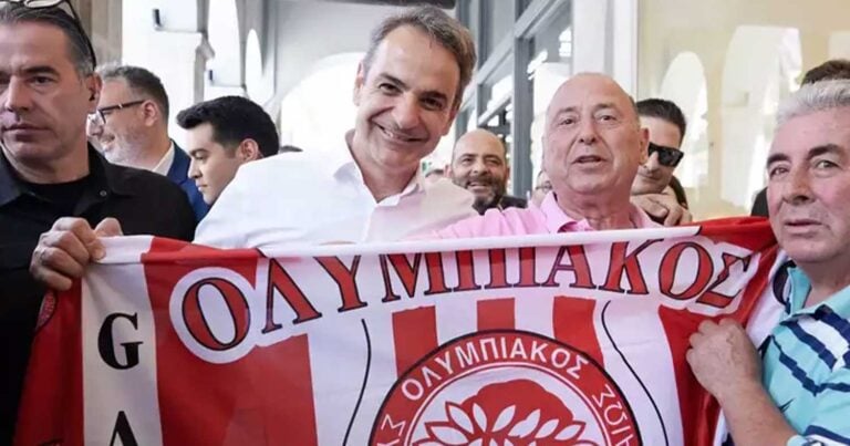 Ο Κυριάκος Μητσοτάκης κρατάει χαμογελαστός τη σημαία του Ολυμπιακού