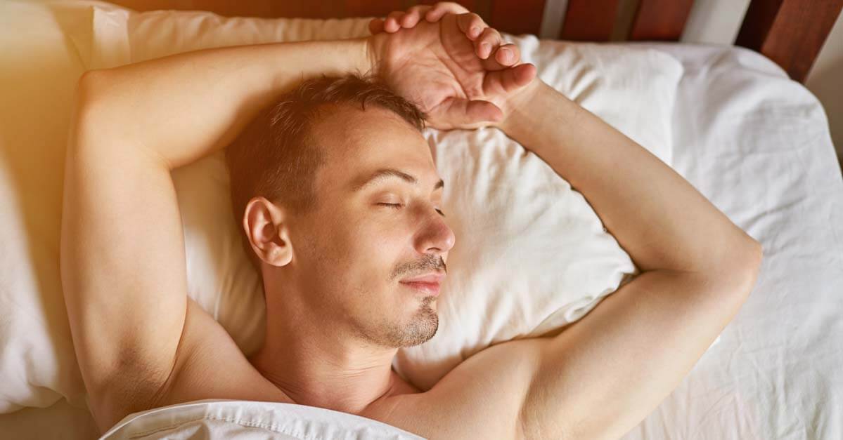one young men sleeping in bed with arms above head