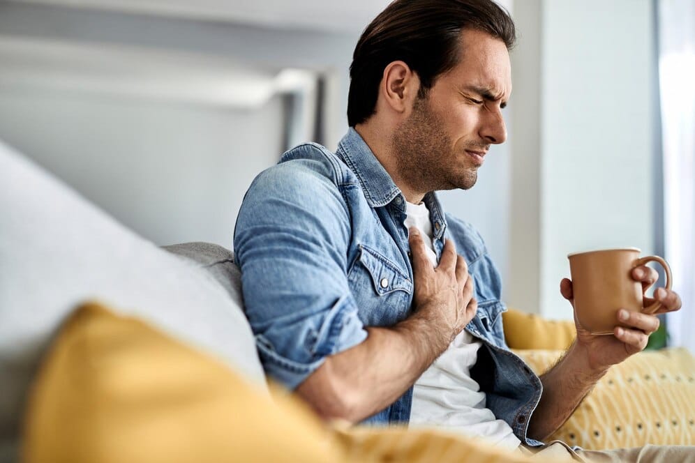 young man feeling sick holding his chest pain while drinking tea living room 637285 5913