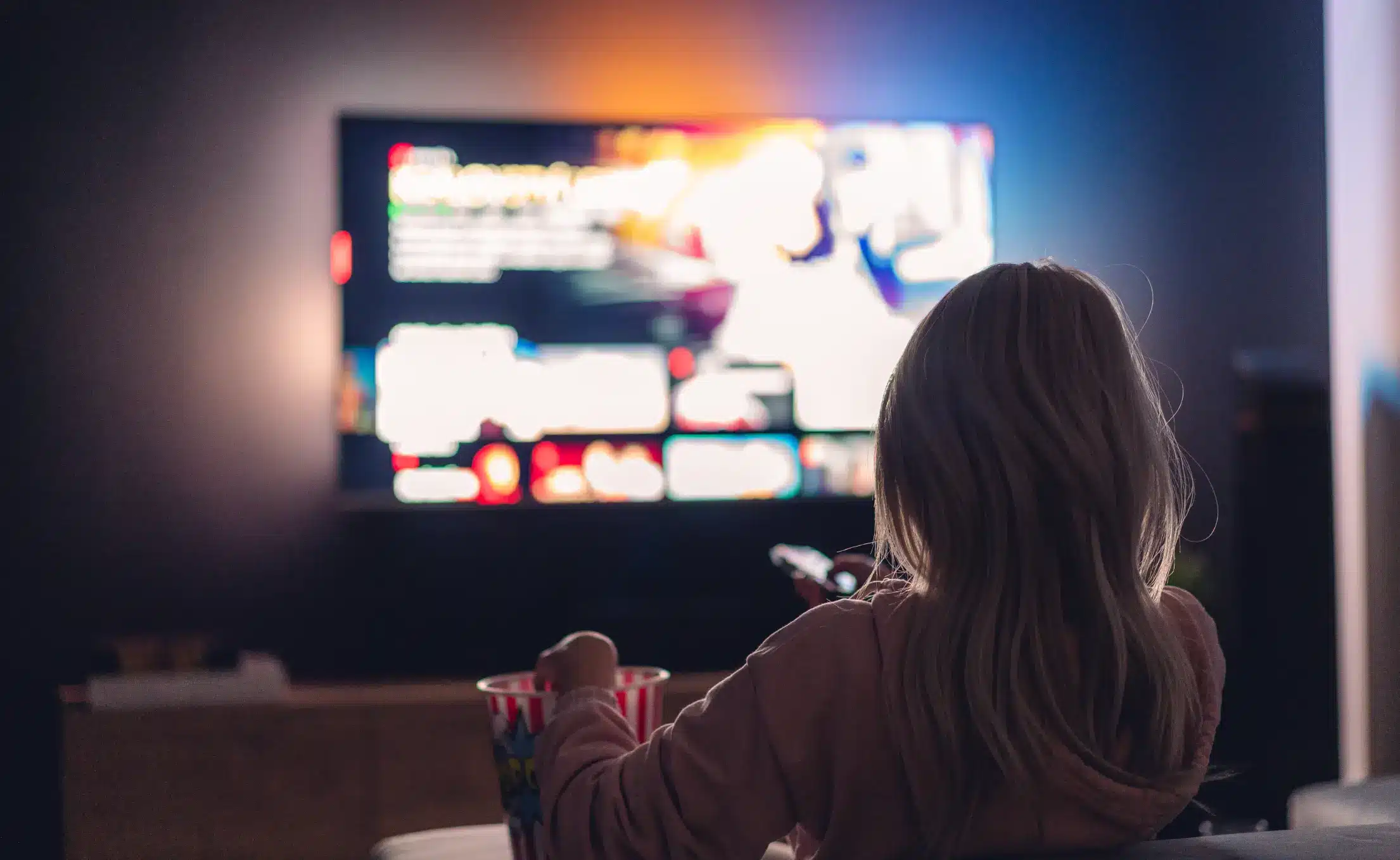 young woman watching tv and eating popcorn at night free photo