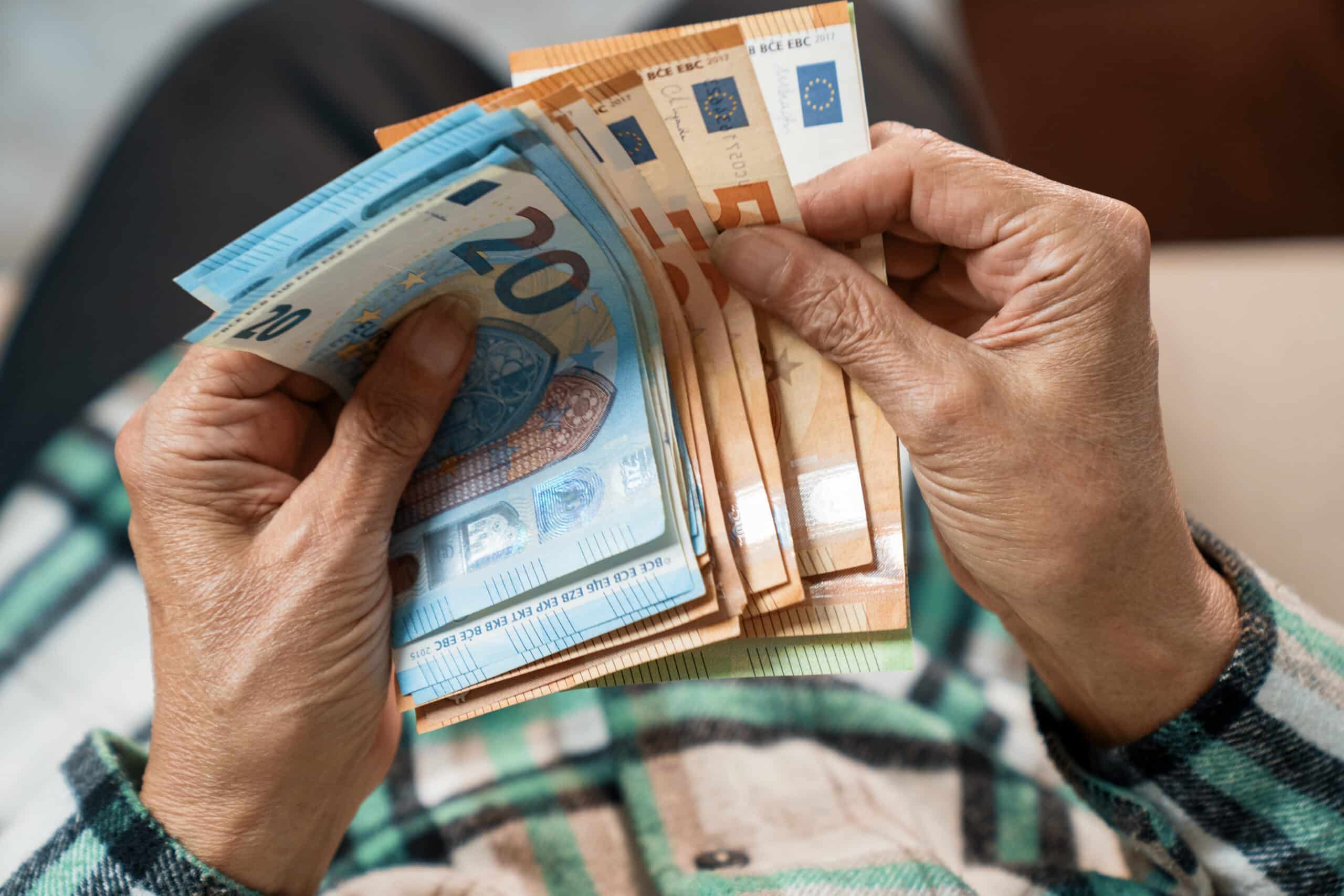close up of elderly womans hands holding a stack of euro banknotes 1 scaled
